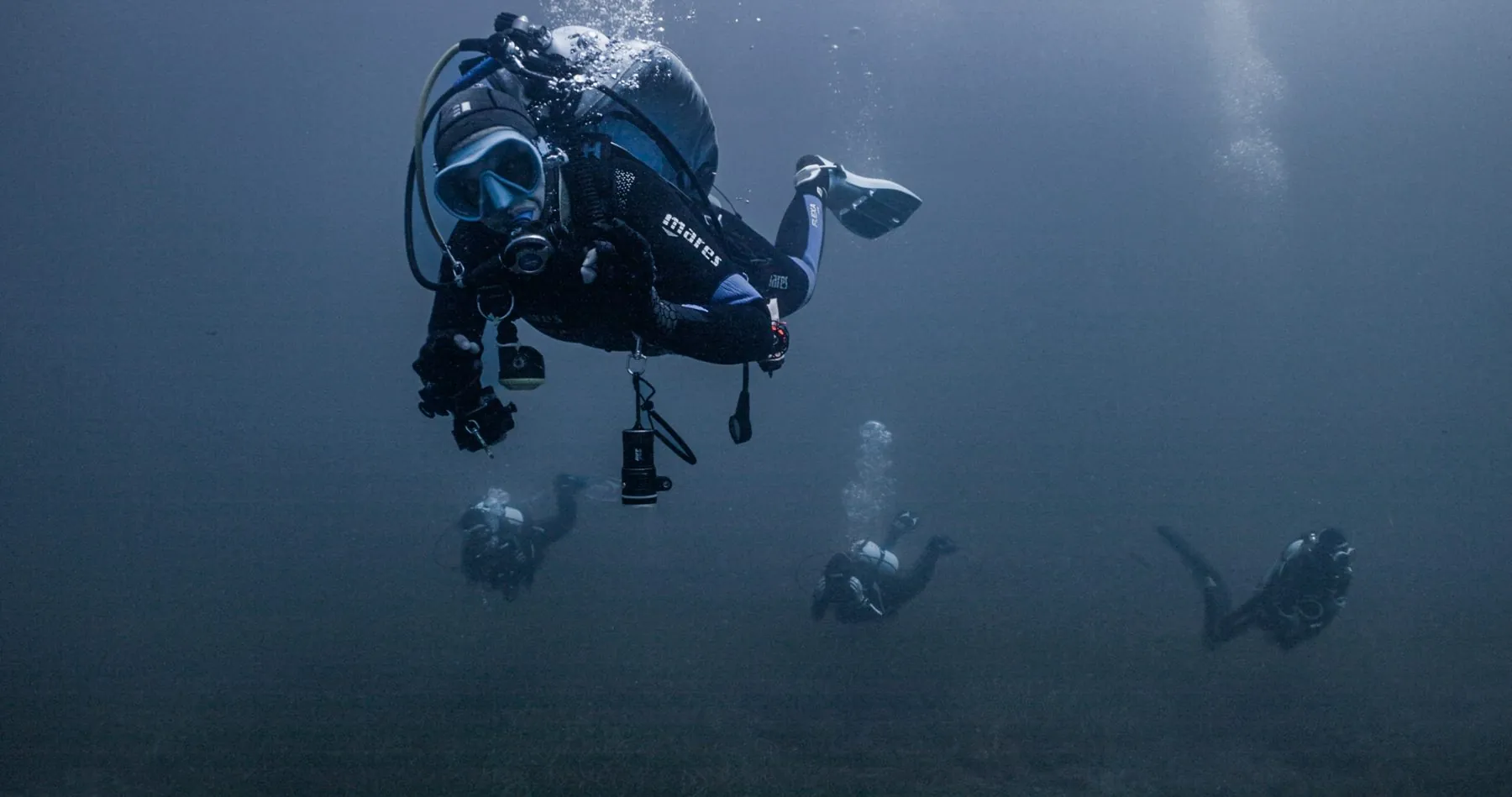 A diver descending through blue water with other divers below