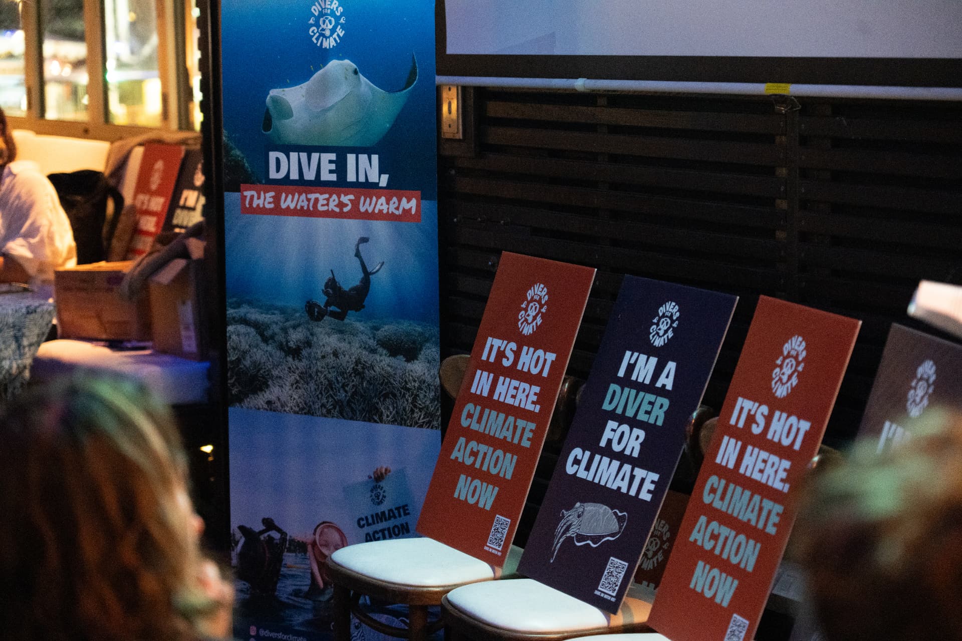 Divers for Climate roll-up banner and campaign signs resting on chairs at Cairns Dive Industry Night